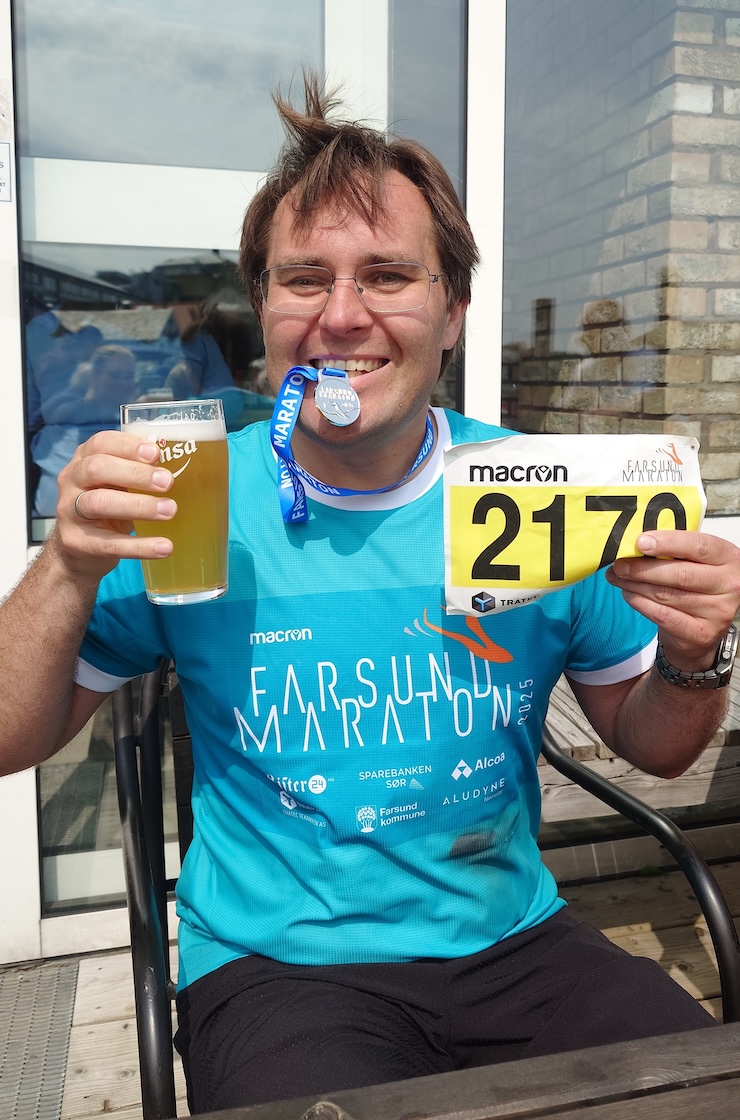 A picture of me after completing the half marathon, holding a beer, my start number, and the medal between my teeth